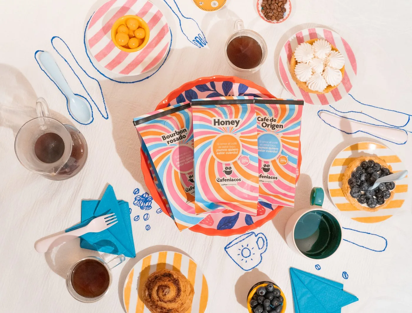 Mesa servida con las tres bolsas de café Cafeniacos, tazas y postres